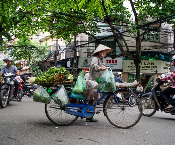 A woman pushing her bike of produce across a busy intersection in Hanoi, Vietnam.